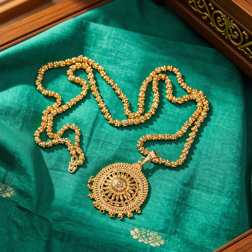 An ornate gold pendant necklace with a detailed circular pendant and matching chain, displayed on a rich teal silk fabric inside a wooden box.