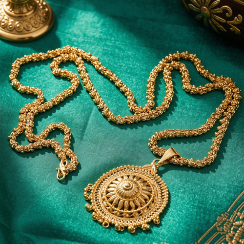 An ornate gold pendant necklace with a detailed circular sunburst design, displayed on a rich teal fabric background with traditional decorative props.