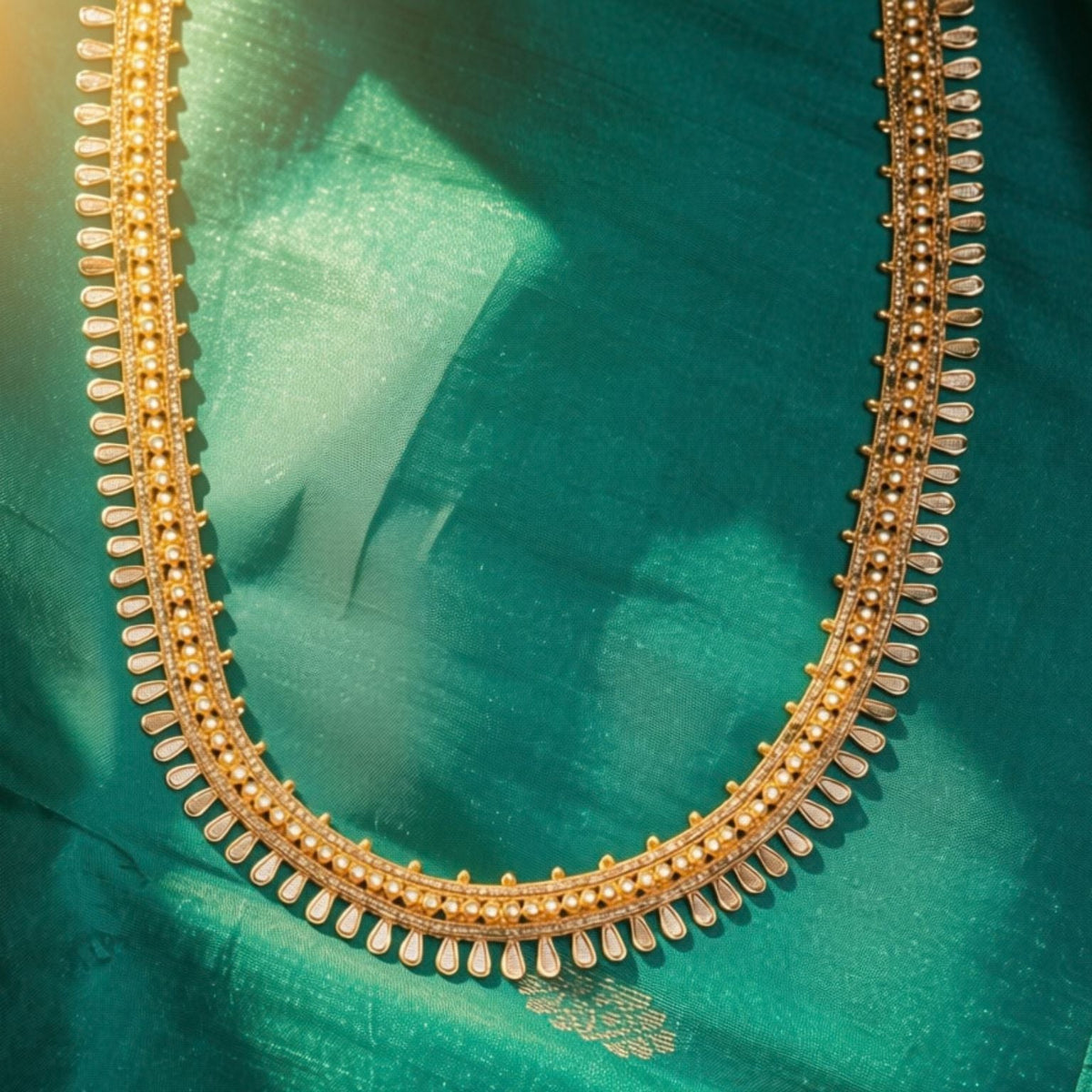 A close-up of a gold-toned traditional necklace laid on a rich teal-green fabric background.