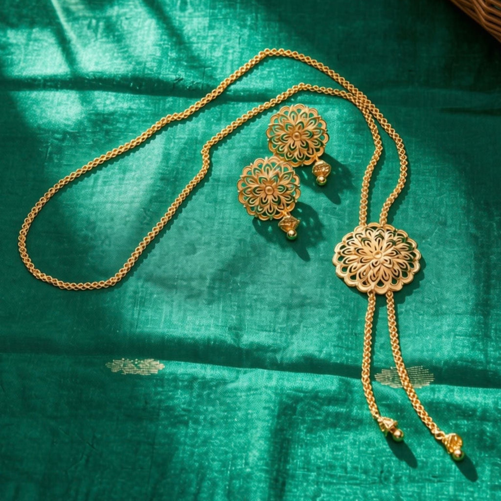 Gold-toned jewelry set including a necklace, earrings, and a matching waist chain laid out on a rich emerald green fabric background.