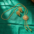 Gold-toned jewelry set including a necklace, earrings, and a matching waist chain laid out on a rich emerald green fabric background.