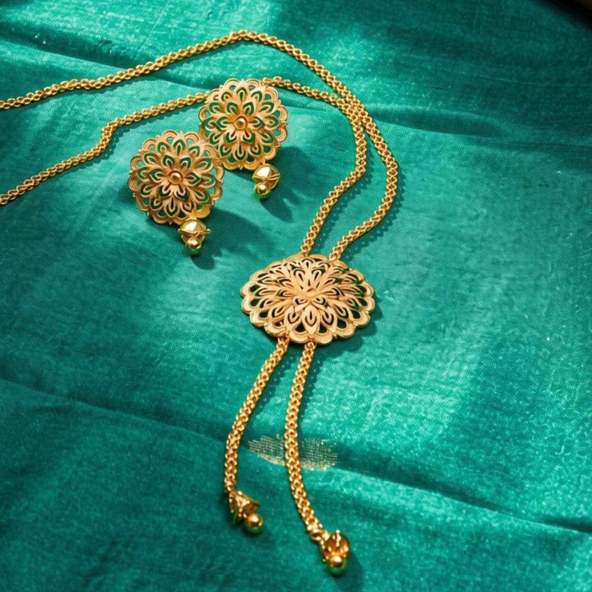 Gold-toned traditional jewelry set including a necklace, matching earrings, and a decorative pendant, arranged on a rich teal fabric background.