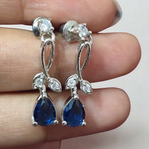 Silver earrings with blue gemstones held between fingers on a white background