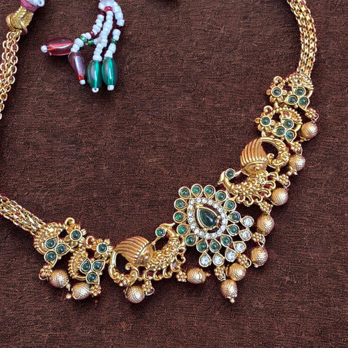 Antique gold peacock temple necklace set with green stones and matching earrings on maroon background