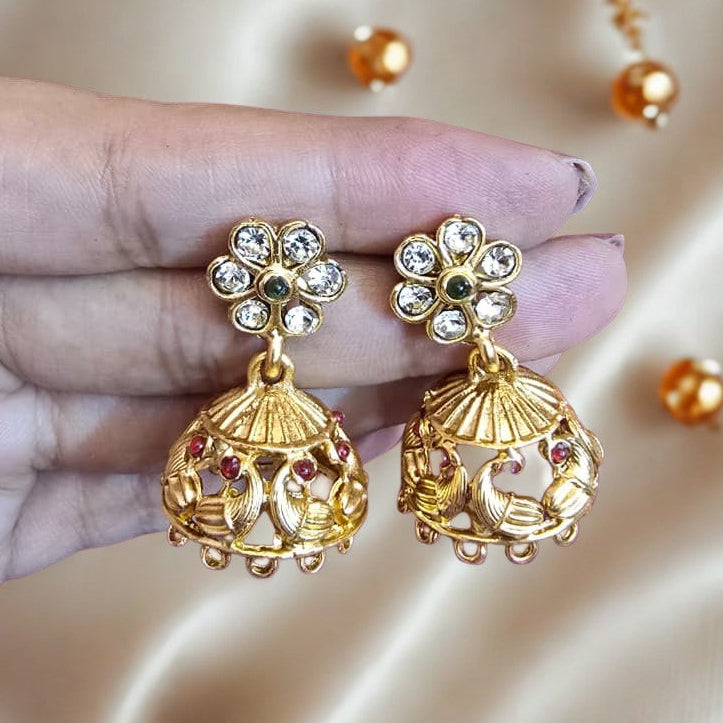 Gold earrings with gemstones held by a hand on a satin background