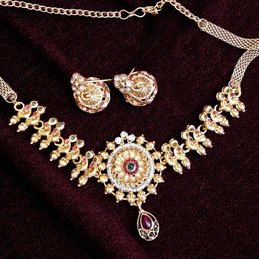 Antique gold floral temple necklace set with ruby and green stones and matching earrings on maroon background