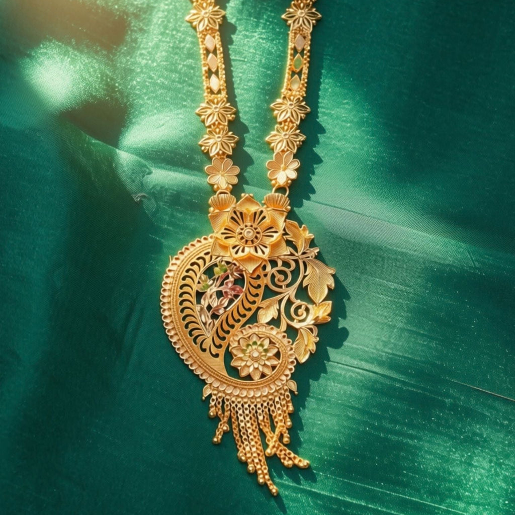 An ornate gold-toned traditional necklace with a large filigree pendant, photographed against a rich green satin fabric background.