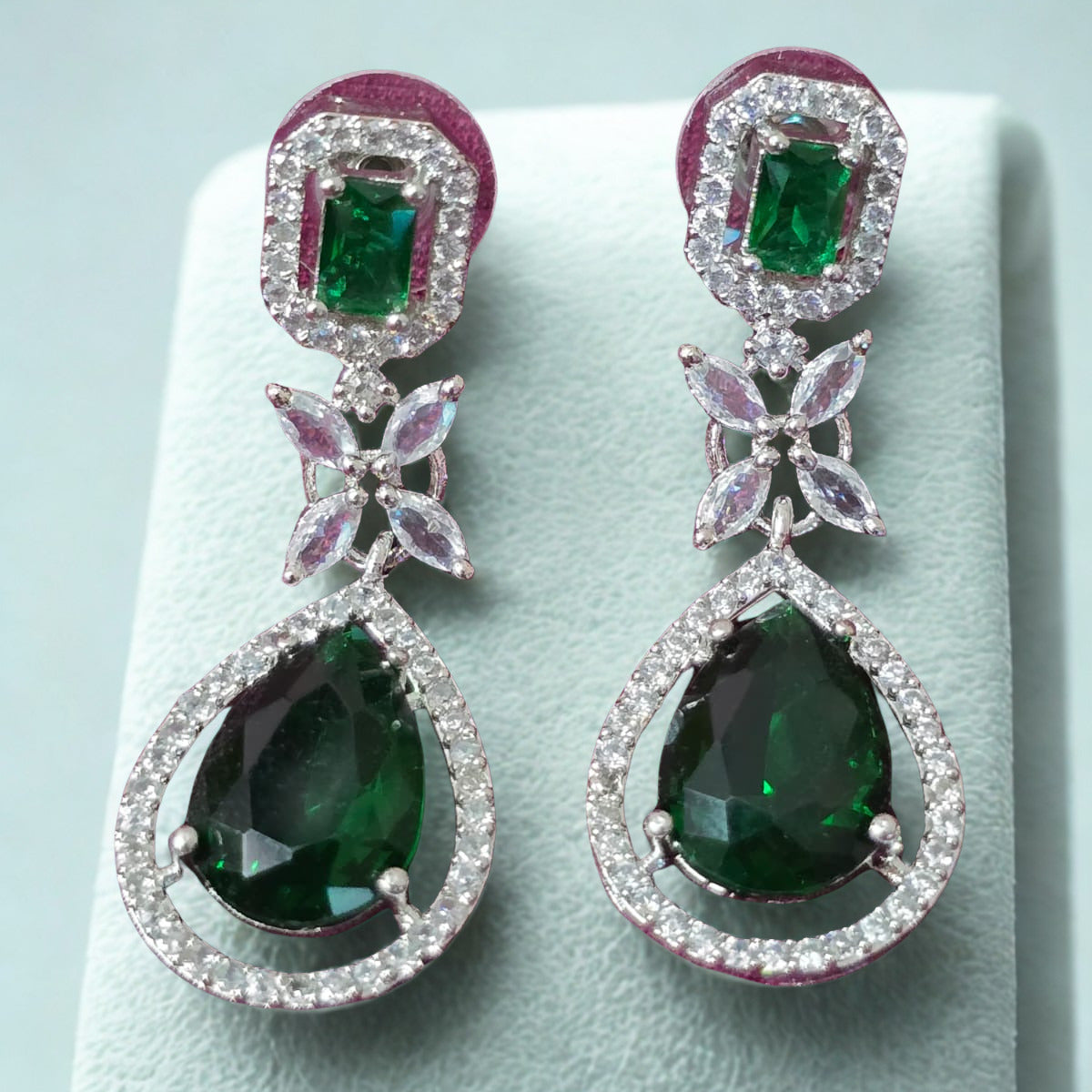 Pair of earrings with green gemstones on a light blue background