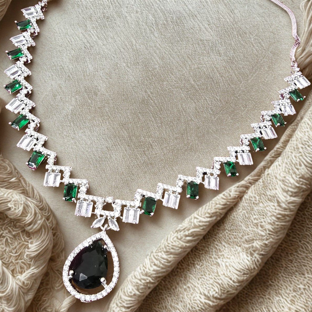 Delicate silver bracelet with green and black gemstones on beige fabric