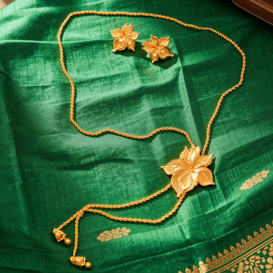 A gold jewelry set featuring a necklace and matching earrings with lotus flower motifs, displayed on a rich green silk fabric with traditional border details.